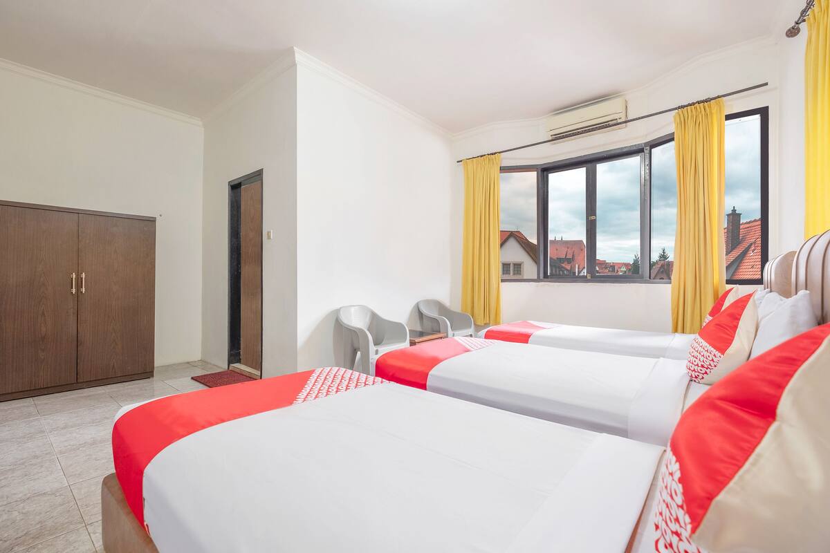 A hotel room with two beds, a wardrobe, a window with curtains, and a view of buildings outside.