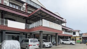 Un hotel con entrada cubierta, varios coches estacionados al frente y una motocicleta cerca.