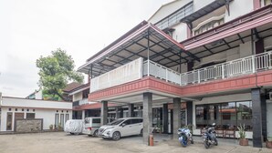 Un hotel con entrada cubierta, varios vehículos estacionados afuera y un balcón con barandilla.