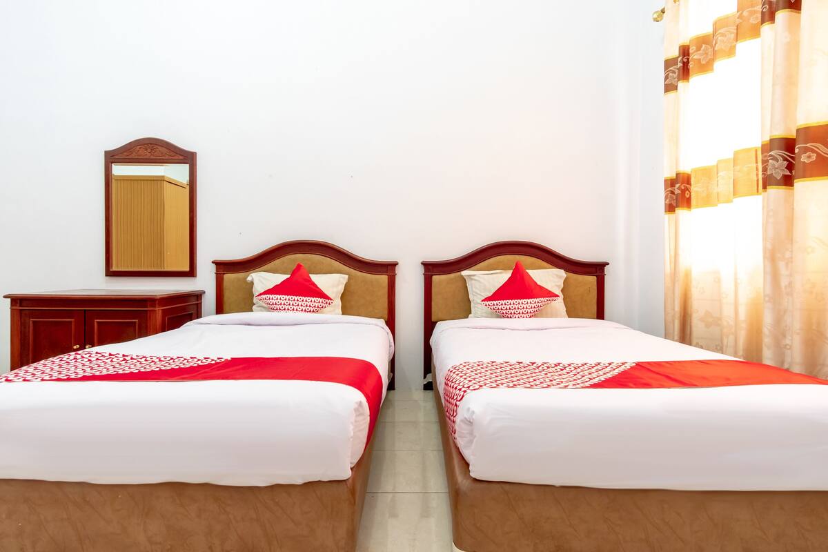 A hotel room with two beds, each with red and white bedding, a wooden headboard, and a mirror on the wall.