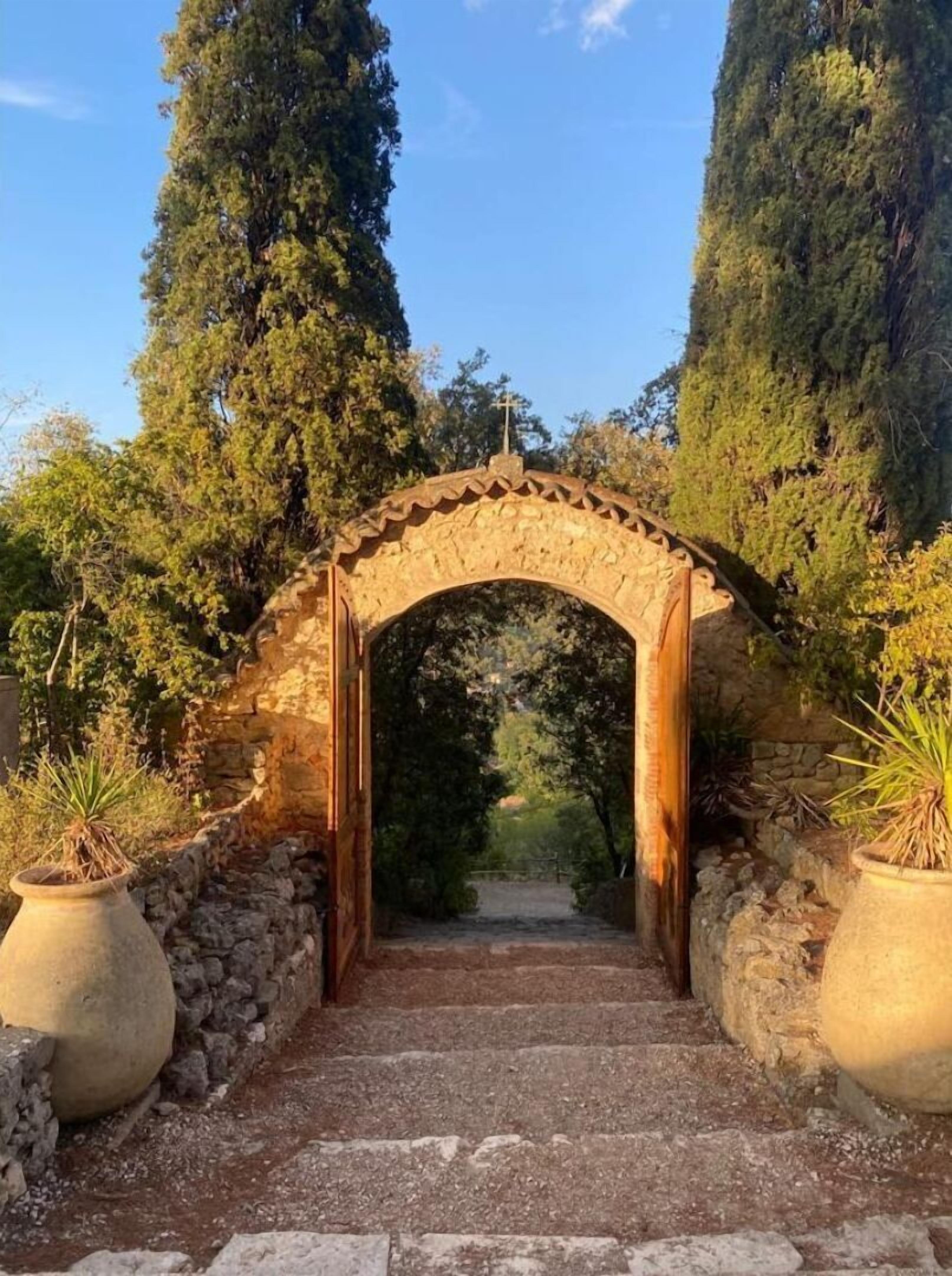 A stone archway leading into a garden with potted plants on either side.