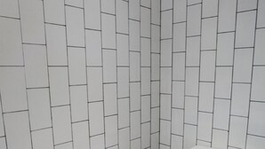 Ein kleines Badezimmer mit weißen Fliesenwänden und einem gemusterten Boden.