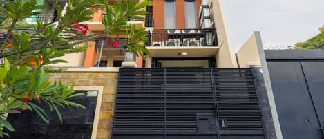 A modern two-story residential building with balconies, a gated entrance, and a view of the surrounding area.