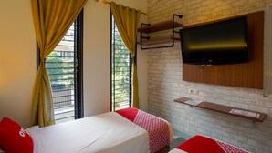 Ein Hotelzimmer mit zwei Betten, einem an einer Ziegelwand montierten Fernseher und einem Fenster mit Vorhängen.