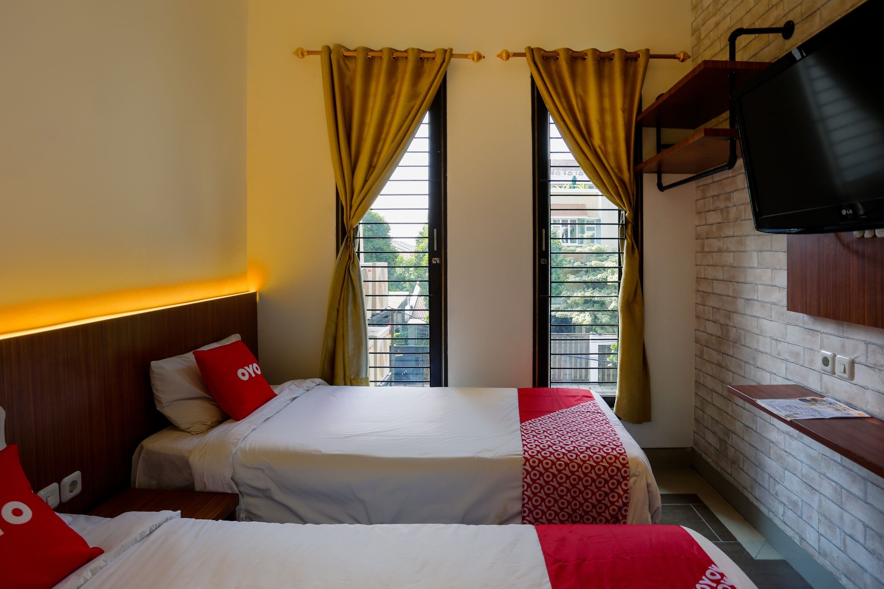 A hotel room with two beds, a TV mounted on the wall, and a window with curtains.