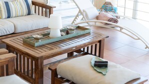 A wooden table with a tray, a candle, and decorative items. There is a white sofa with striped pillows and a white chair with a rolled-up towel.