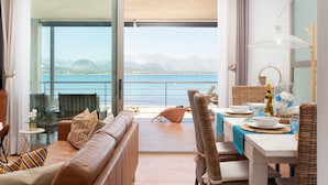 A balcony with a view of the sea and mountains, furnished with a sofa, chairs, and a dining table.