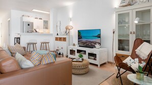 A modern living room with a sofa, TV, and a dining area with chairs and a table.