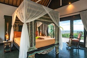 A four-poster bed with a canopy, a nightstand with a lamp, and a view of the outdoors. - Villa Jempiring (Banjar)