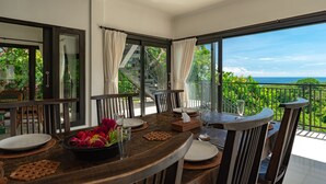 A dining area with a table set for four, large windows, and a view of the ocean. - Villa Jempiring (Banjar)
