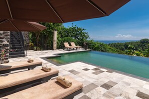 A poolside area with lounge chairs, a stone staircase, and a view of the ocean. - Villa Jempiring (Banjar)