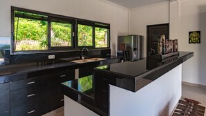 A modern kitchen with a black countertop, a sink, and a window with a view of greenery. - Villa Jempiring (Banjar)