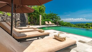 A poolside area with lounge chairs, a stone wall, and a view of the ocean. - Villa Jempiring (Banjar)