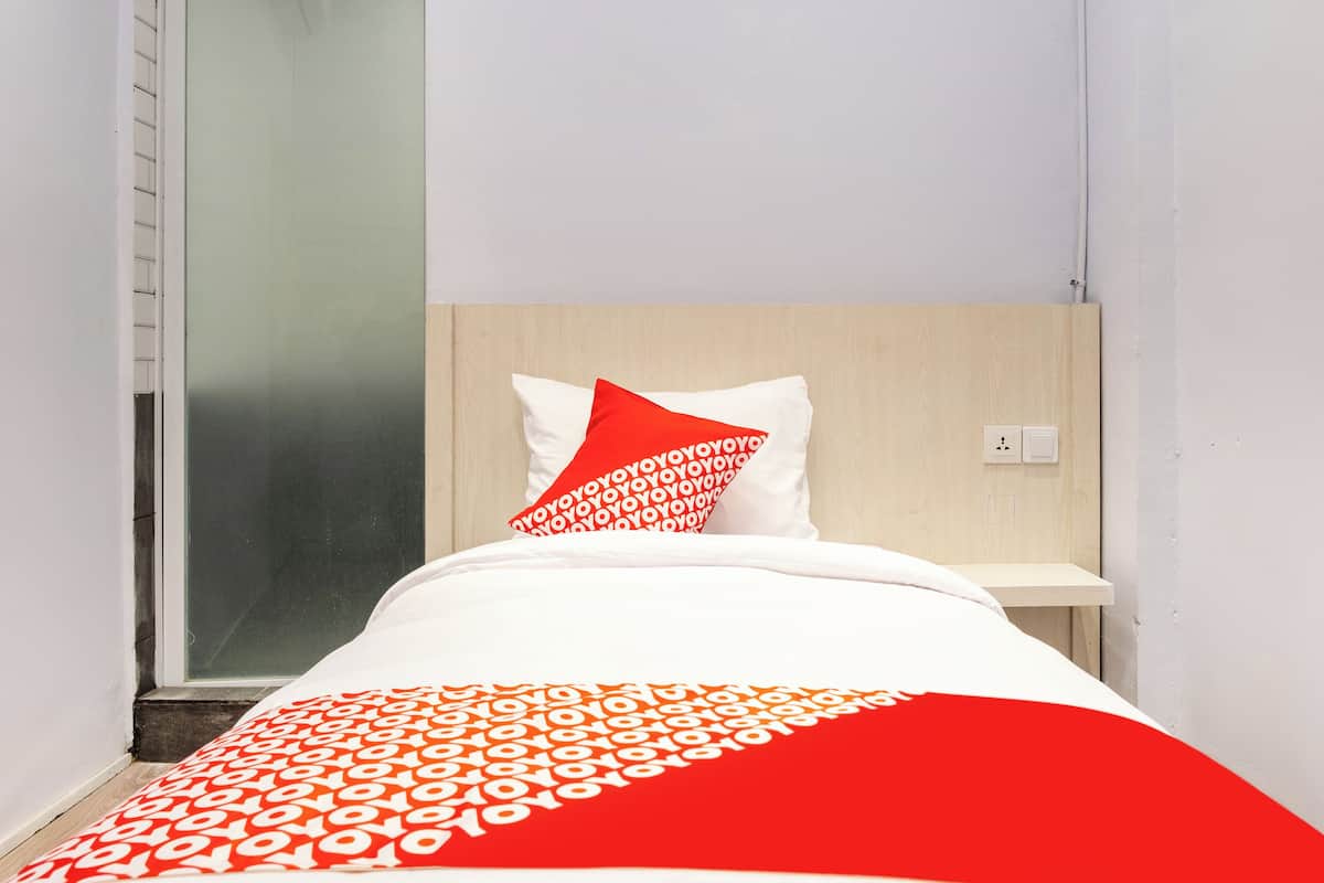 A hotel room with a bed, a nightstand, a wooden headboard, a glass shower door, and a white wall.