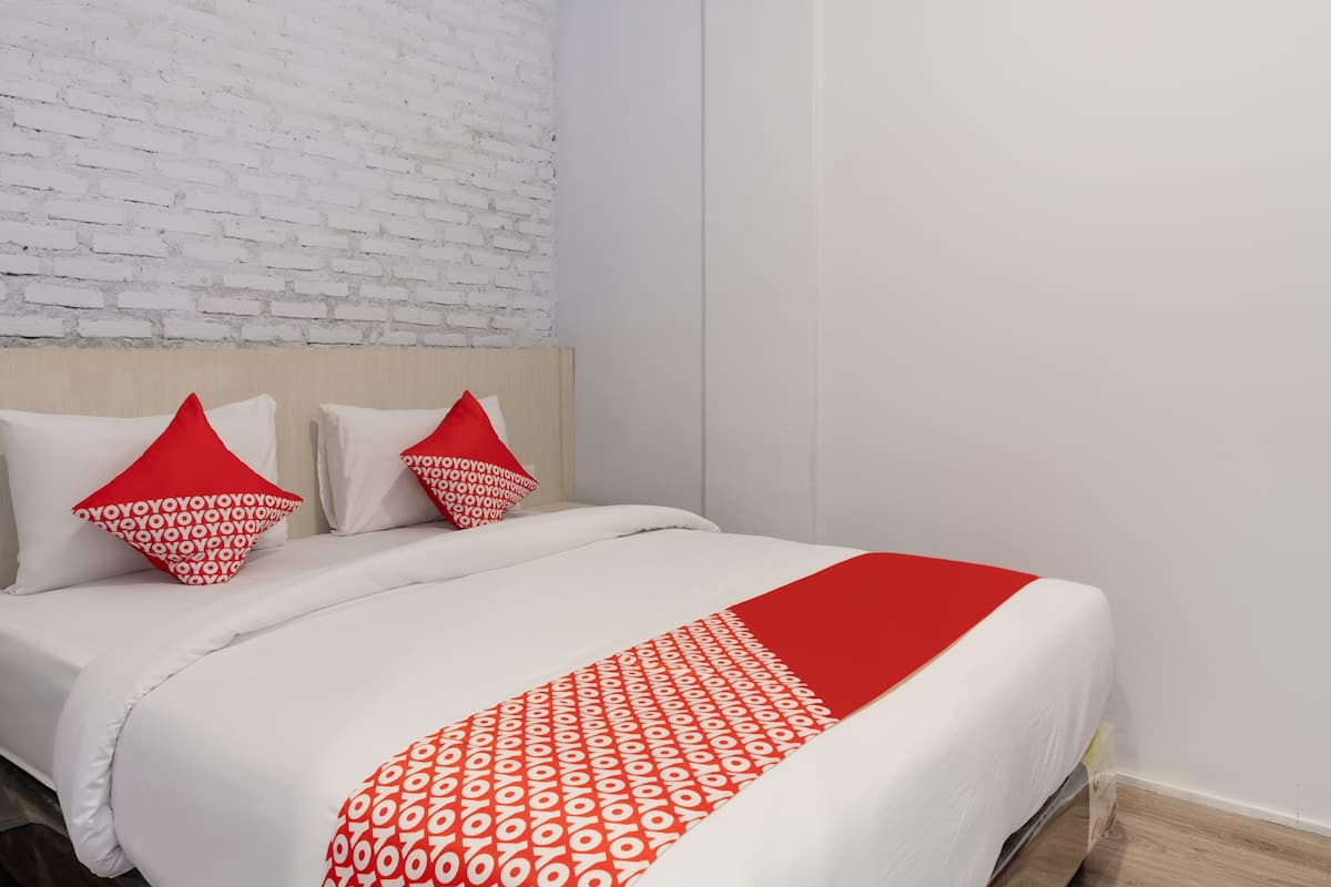 A neatly made bed with white bedding and red accents, a white brick wall, and a wooden floor.