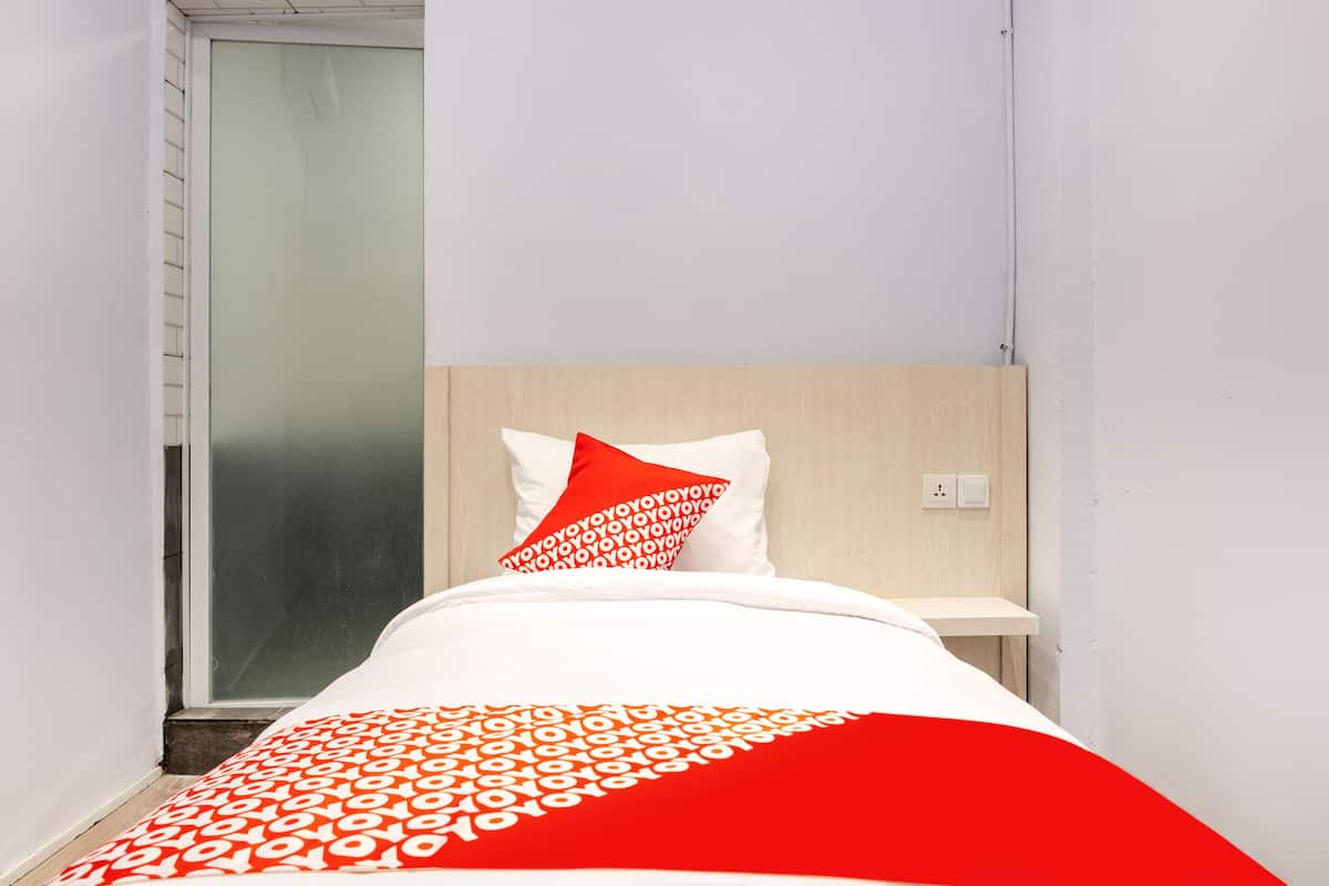 A small, modern bedroom with a bed, a nightstand, and a window with a frosted glass door.