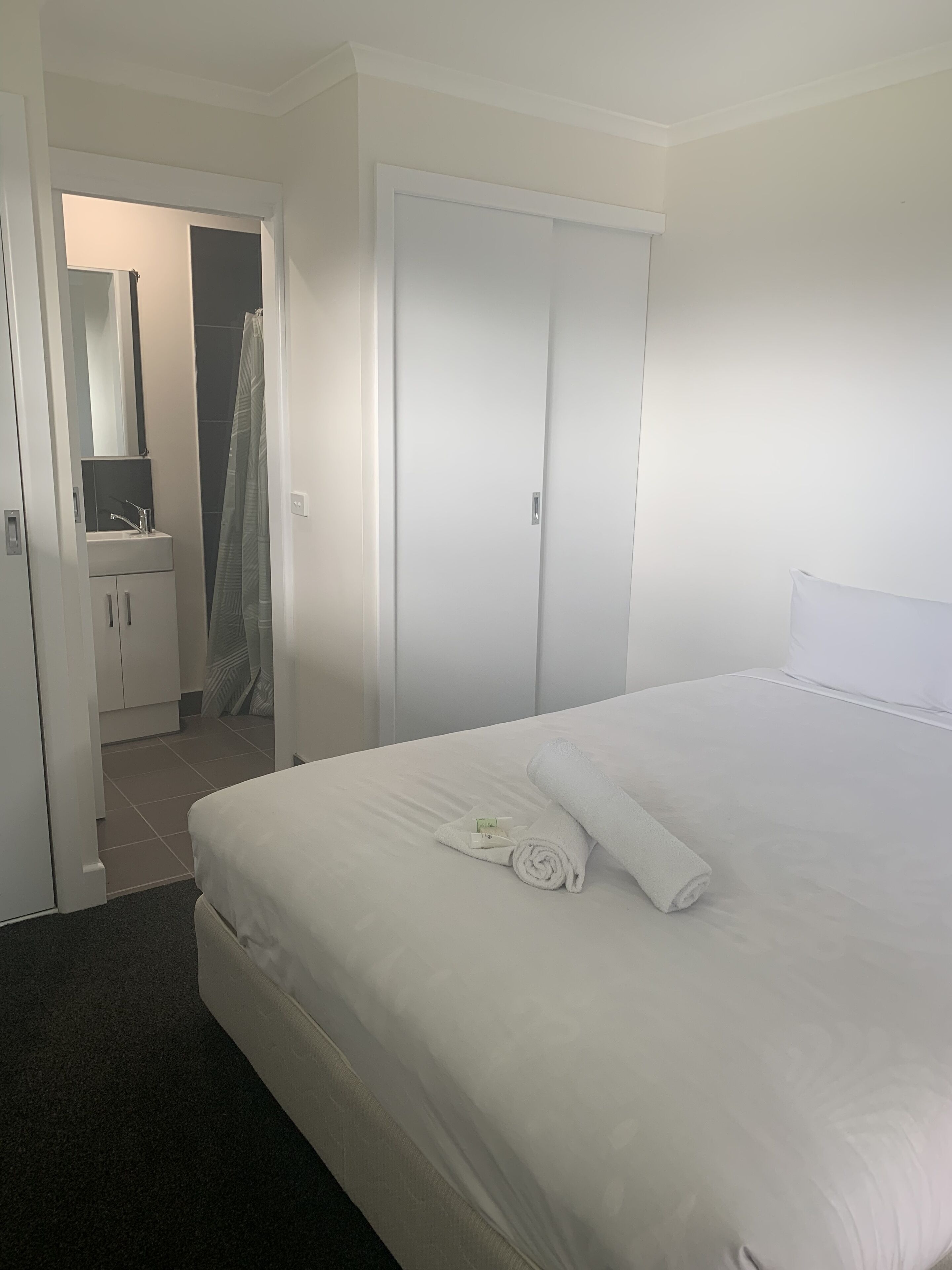 Een hotelkamer met een net opgemaakt bed, een badkamer met een wastafel en spiegel, en een deur naar een andere kamer.