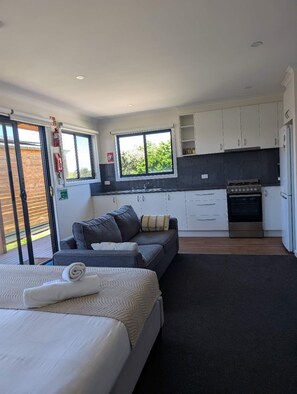 A modern bedroom with a large bed, a sofa, and a dining area with a stove. - Colac Otway Caravan & Cabin Park (Colac West)