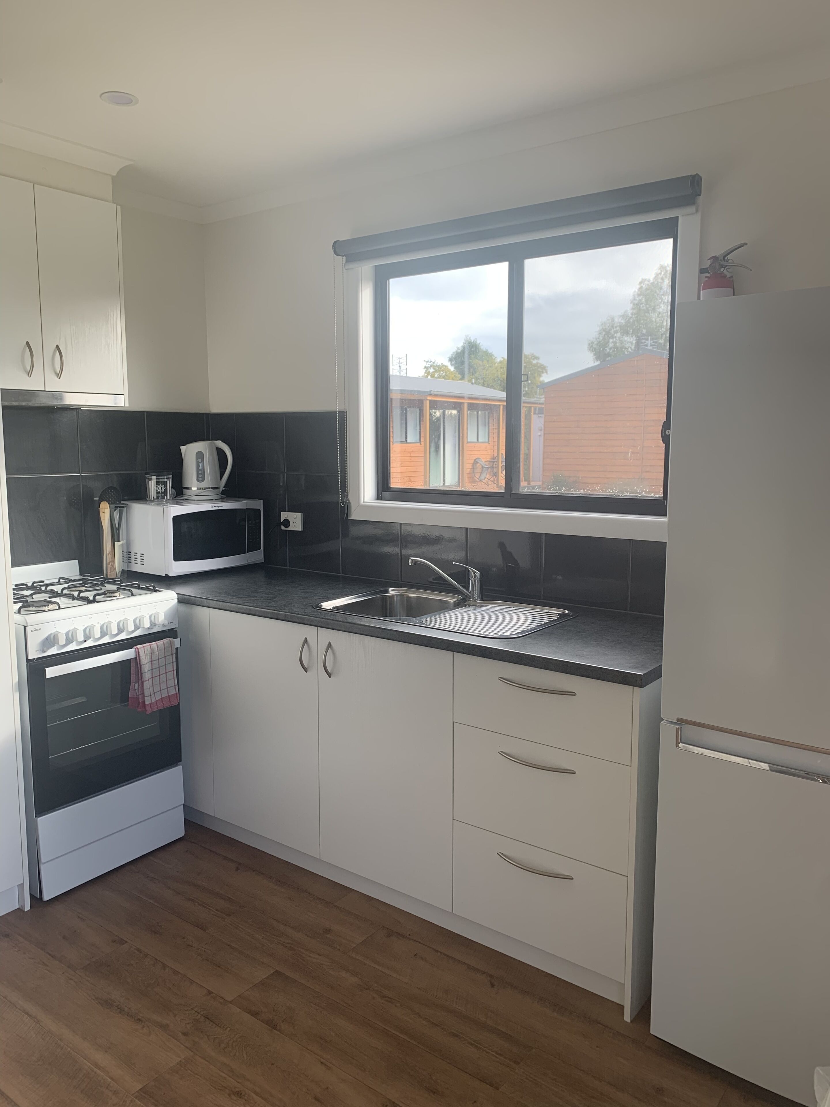 Een moderne keuken met witte kasten, een gasfornuis, een magnetron en een spoelbak.