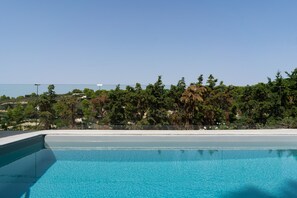 Una piscina azul cristalina con vista a una playa y árboles al fondo.
