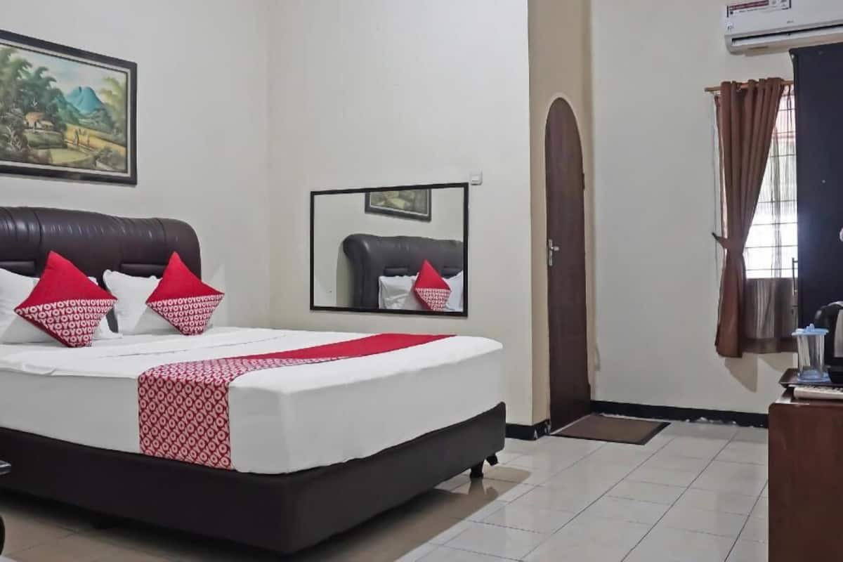 Een hotelkamer met een bed, een spiegel, een deur en een raam met gordijnen.