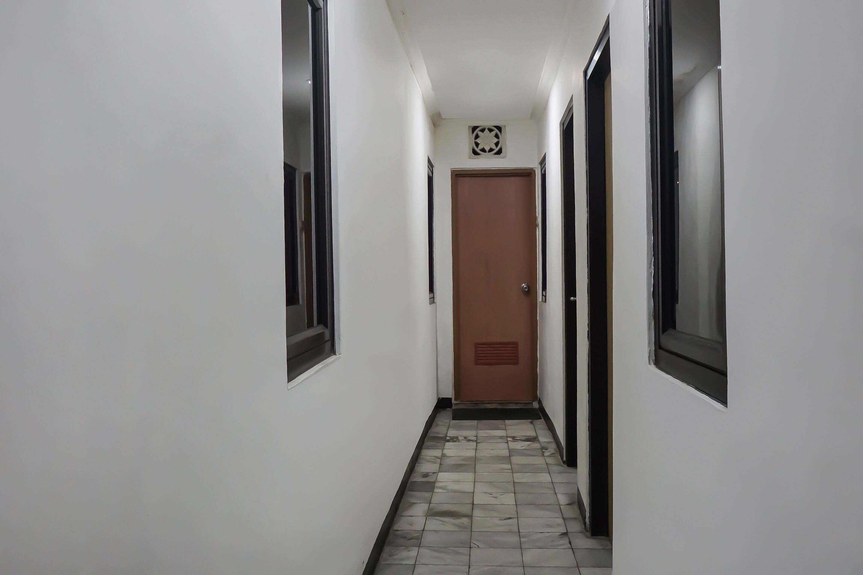 A narrow hallway with white walls, a tiled floor, and a door at the end.