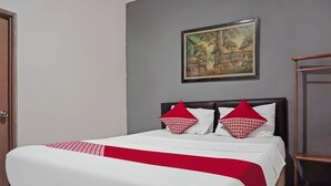 A neatly made bed with a white and red bedspread, two red pillows, and a wooden headboard. A framed painting hangs on the wall above the bed. - Hotel O Bogor Guest House (Bogor)