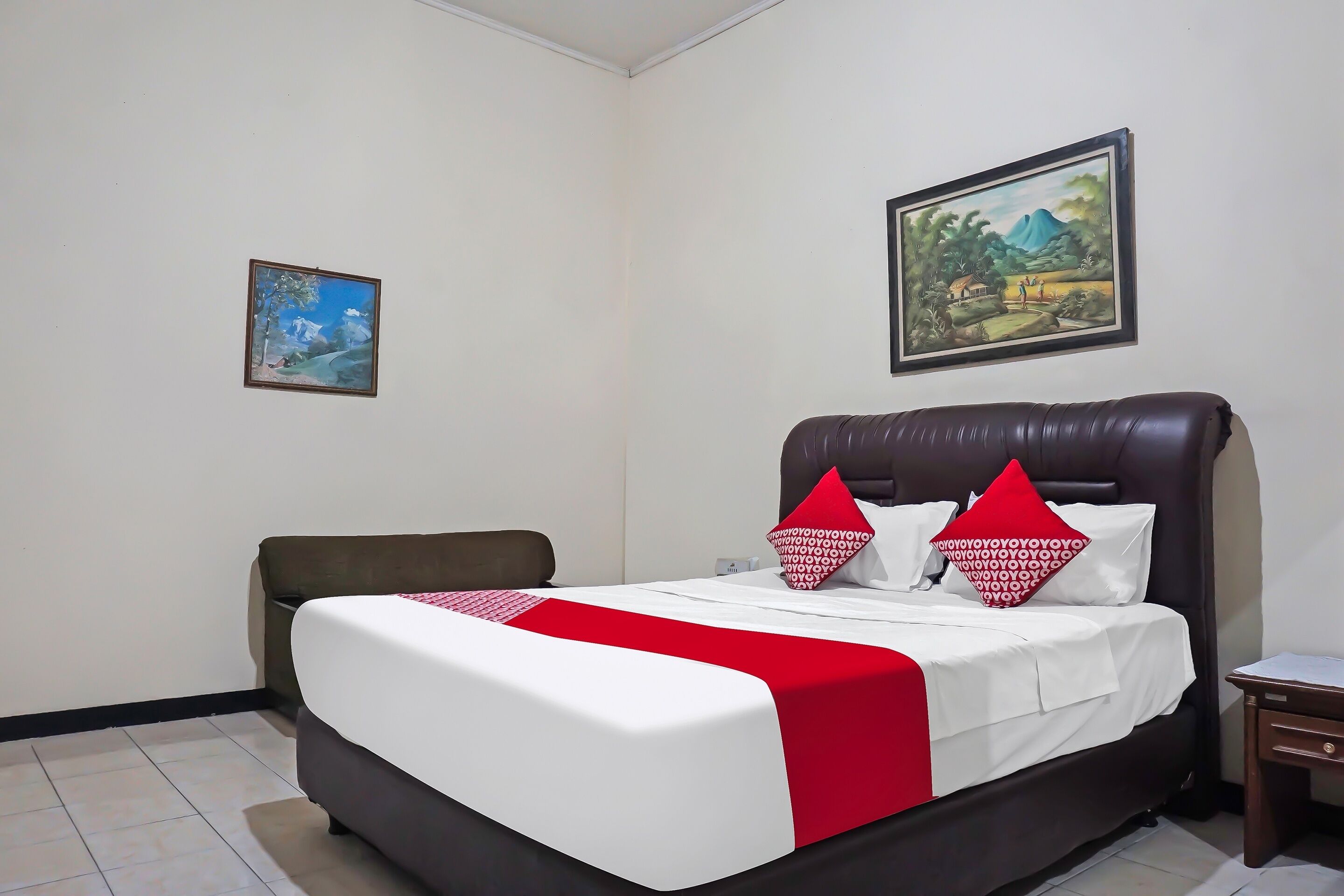 A neatly made bed with a red and white bedspread, two matching pillows, and a headboard.