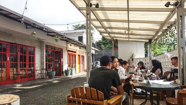 An outdoor café with tables and chairs, a cobblestone street, and buildings with red doors. - Hotel O Bogor Guest House (Bogor)