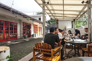 An outdoor café with tables and chairs, a cobblestone street, and buildings with red doors. - Hotel O Bogor Guest House (Bogor)