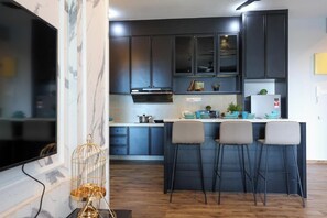 A modern kitchen with dark cabinets, a central island with bar stools, and a flat-screen TV mounted on the wall.