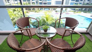A balcony with wicker chairs and a glass table, overlooking a swimming pool and greenery. - Atlantis Residence Premium By I Housing (Malacca City)
