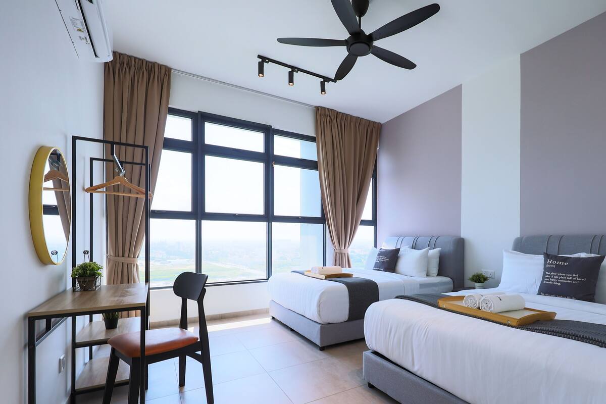 Een moderne hotelkamer met een groot bed, een kleiner bed, een bureau met stoel en een groot raam met gordijnen.