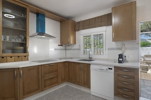 A kitchen with wooden cabinets, a dishwasher, a window with blinds, and a tiled backsplash.