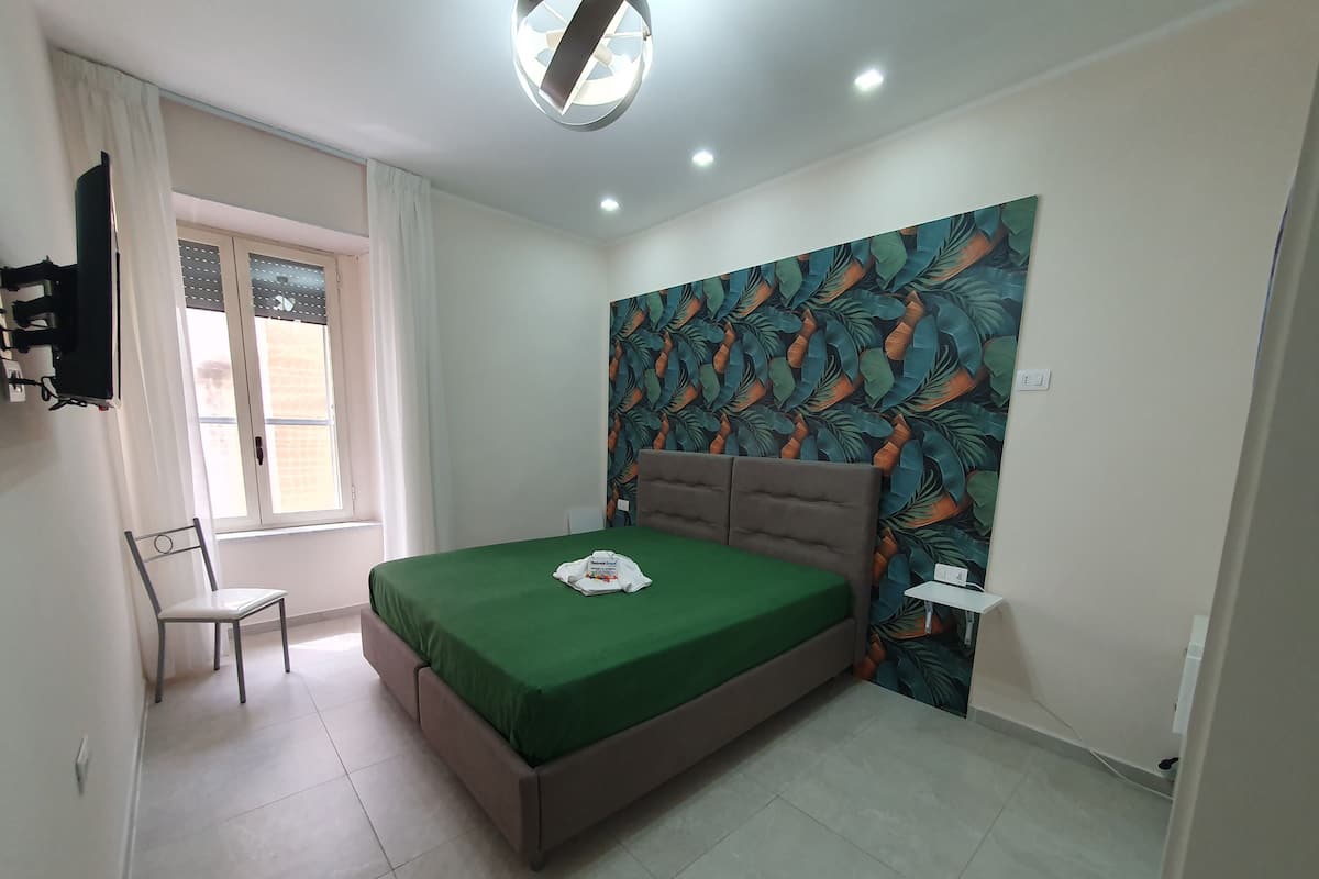 A bedroom with a bed, a chair, a window, and a wall with a leaf pattern.