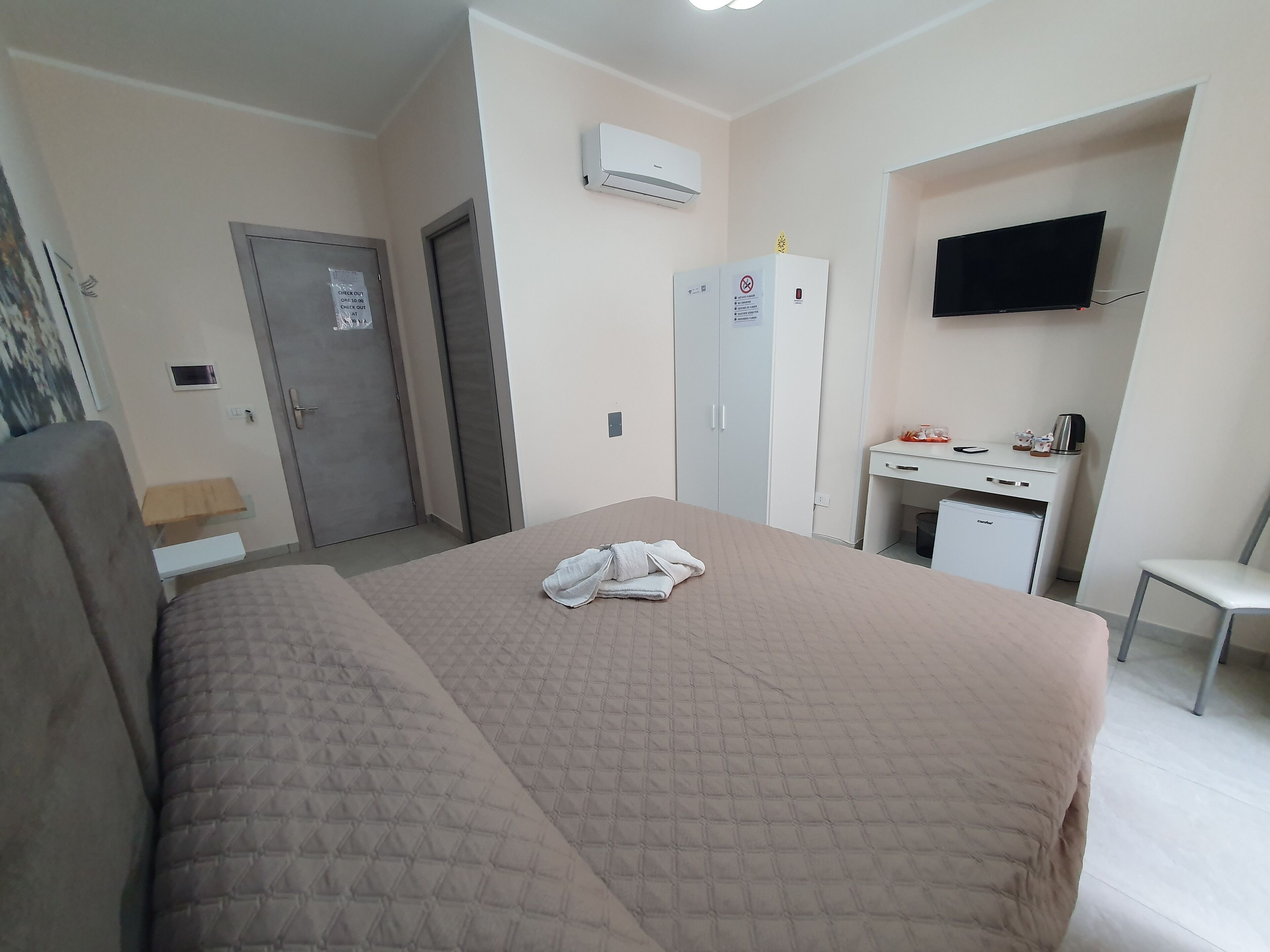 Hotellihuone, jossa on sänky, työpöytä tietokoneella, televisio ja ilmastointilaite.