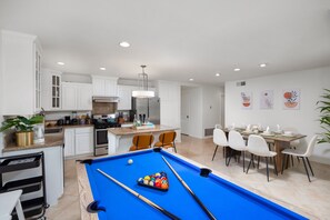 A modern kitchen with white cabinets, a built-in oven, and a dining area with a pool table.