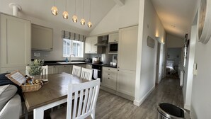 A modern kitchen with white cabinets, a dining table, and hanging pendant lights.