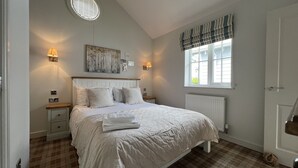 A bedroom with a bed, nightstands, a radiator, a window with curtains, and a wall-mounted artwork.