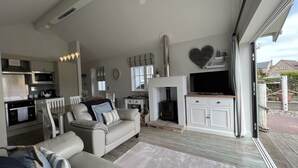 A modern living room with a sofa, TV, fireplace, and kitchen area.