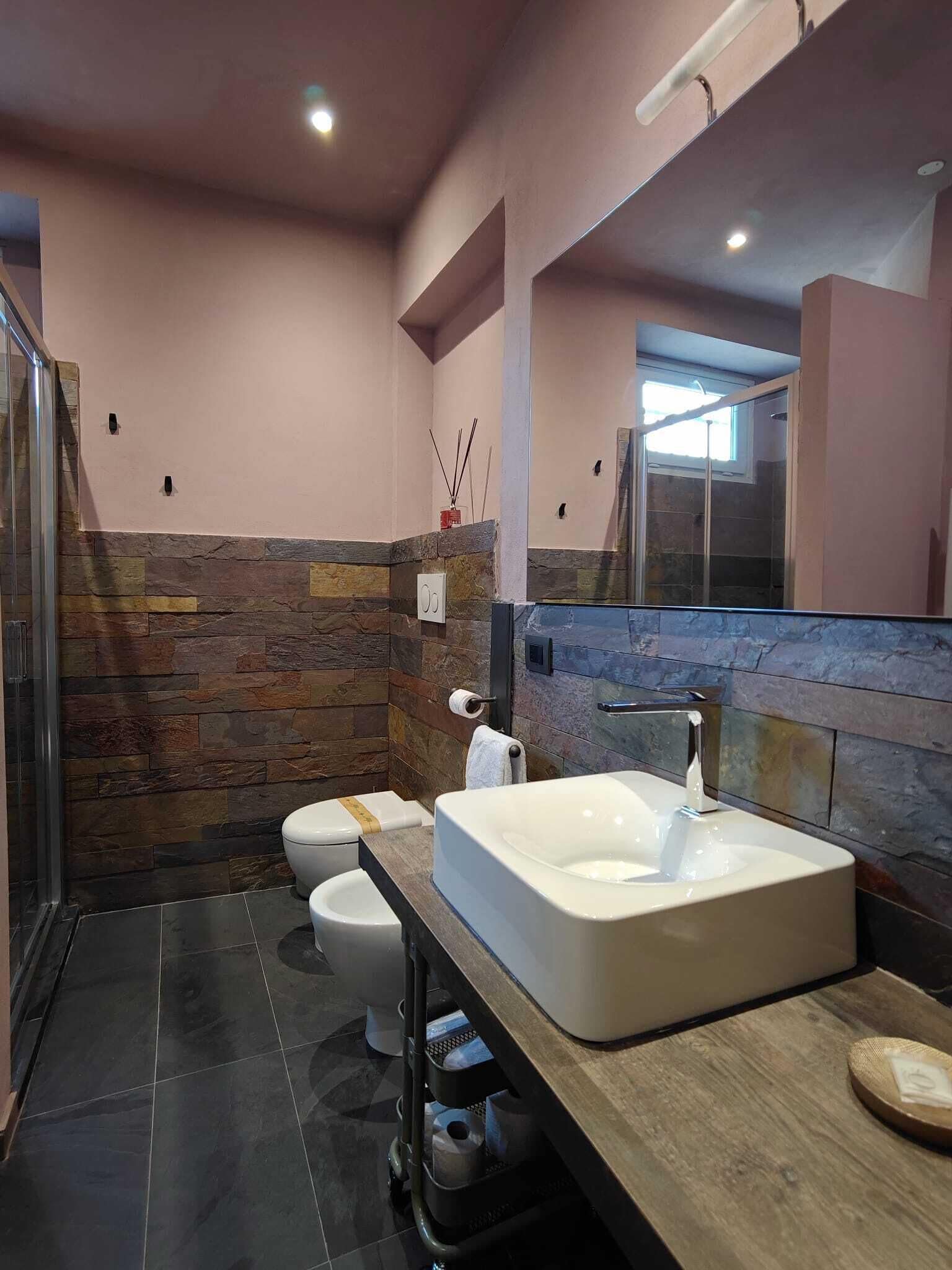 A modern bathroom with a stone accent wall, a large bathtub, a toilet, and a shower area.