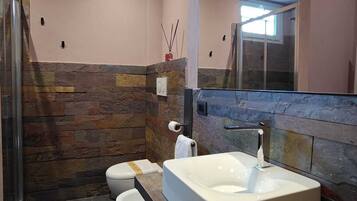 A modern bathroom with a stone accent wall, a large bathtub, a toilet, and a shower area.