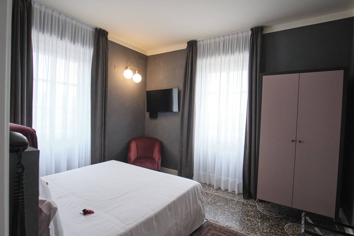 Ein Hotelzimmer mit Bett, Sessel, Kleiderschrank und flachbildfernseher an der Wand.