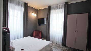 Una habitación de hotel con cama, una silla, armario y televisor de pantalla plana en la pared.