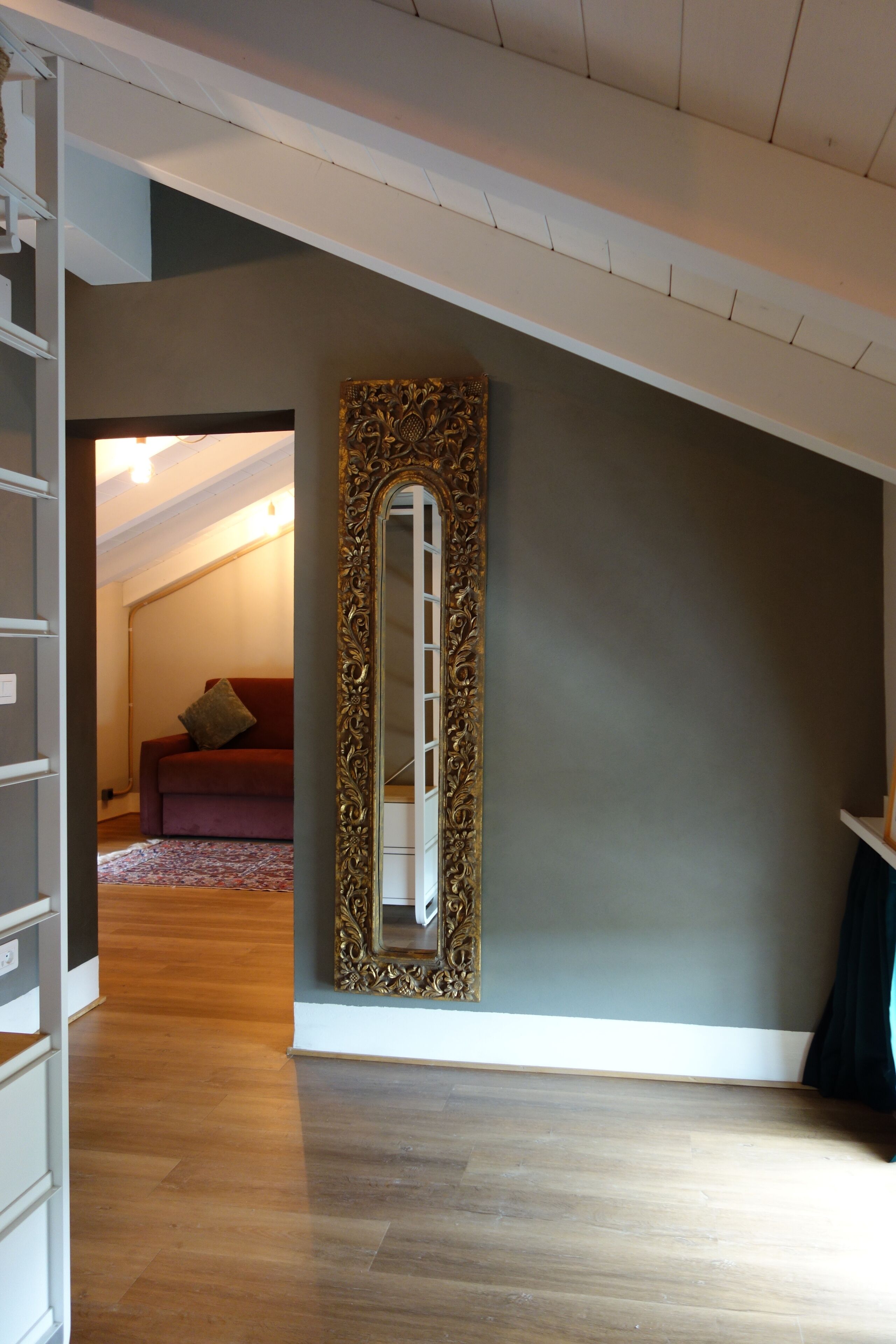 Una habitación con un espejo grande, un sofá rojo y suelo de madera.