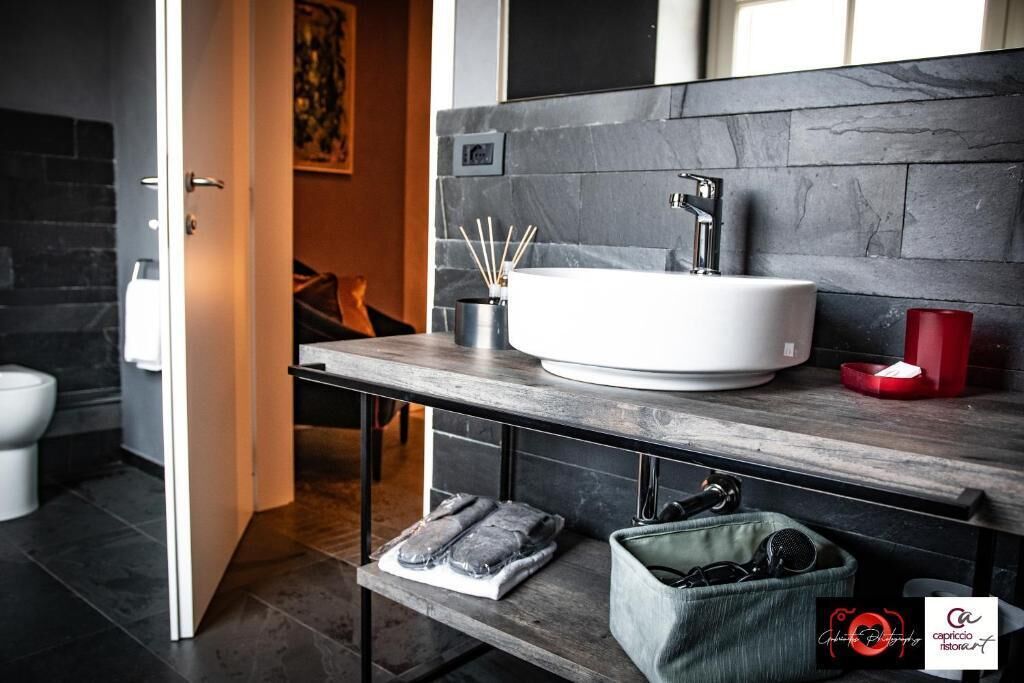 A modern bathroom with a white sink, dark stone backsplash, and a wooden countertop.