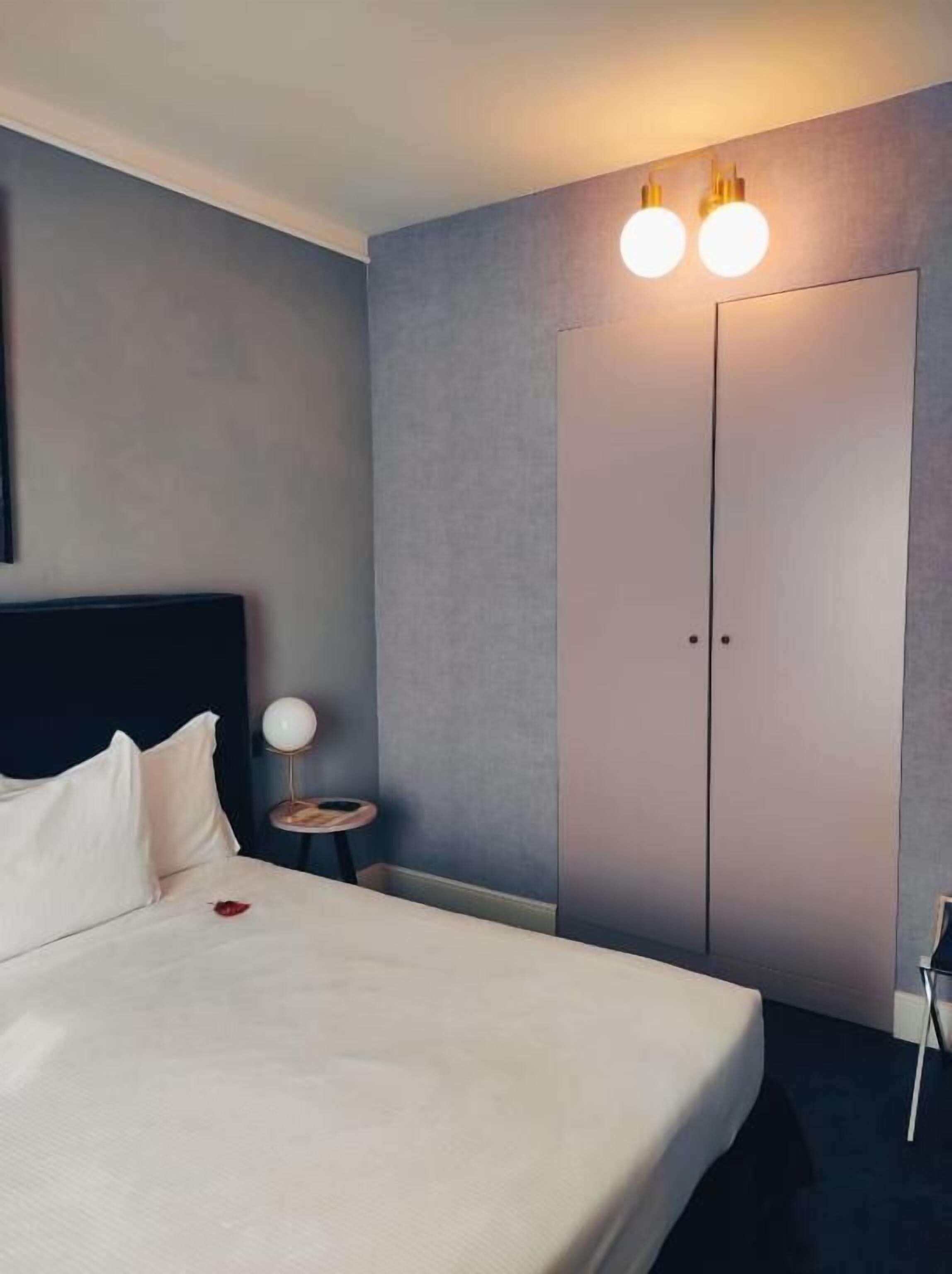 Een hotelkamer met een bed, nachtkastje met lamp en een kledingkast.