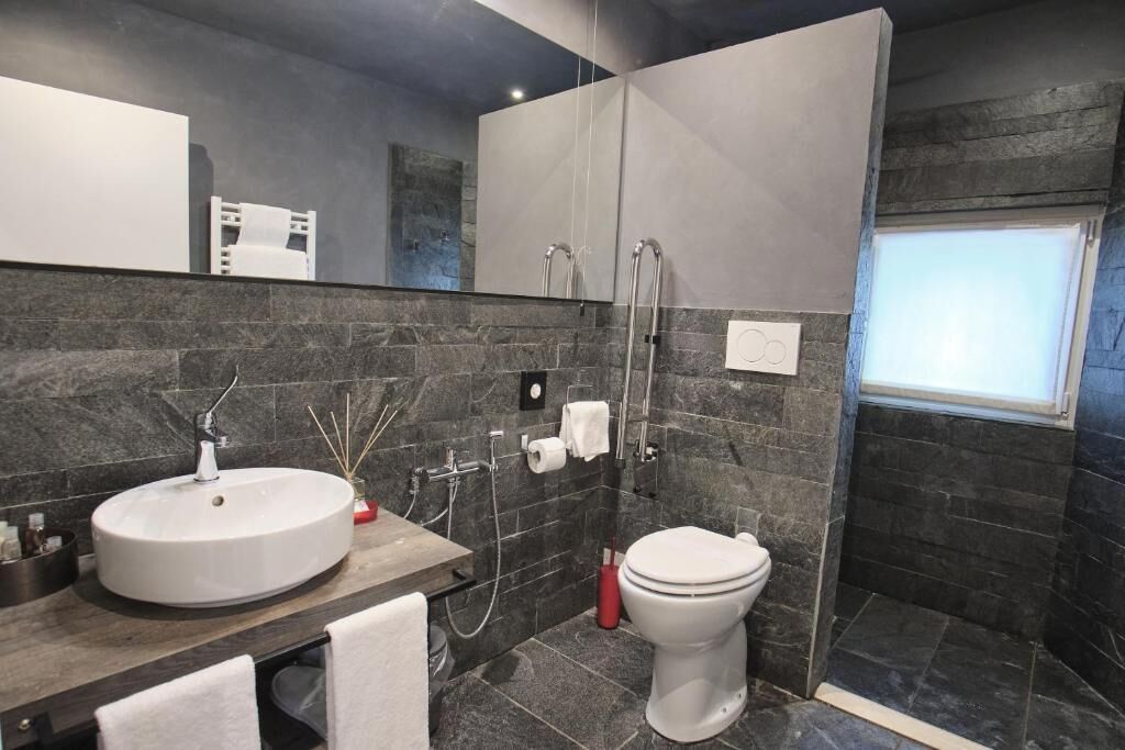 Un baño moderno con un lavabo redondo, inodoro y ducha a ras de suelo.