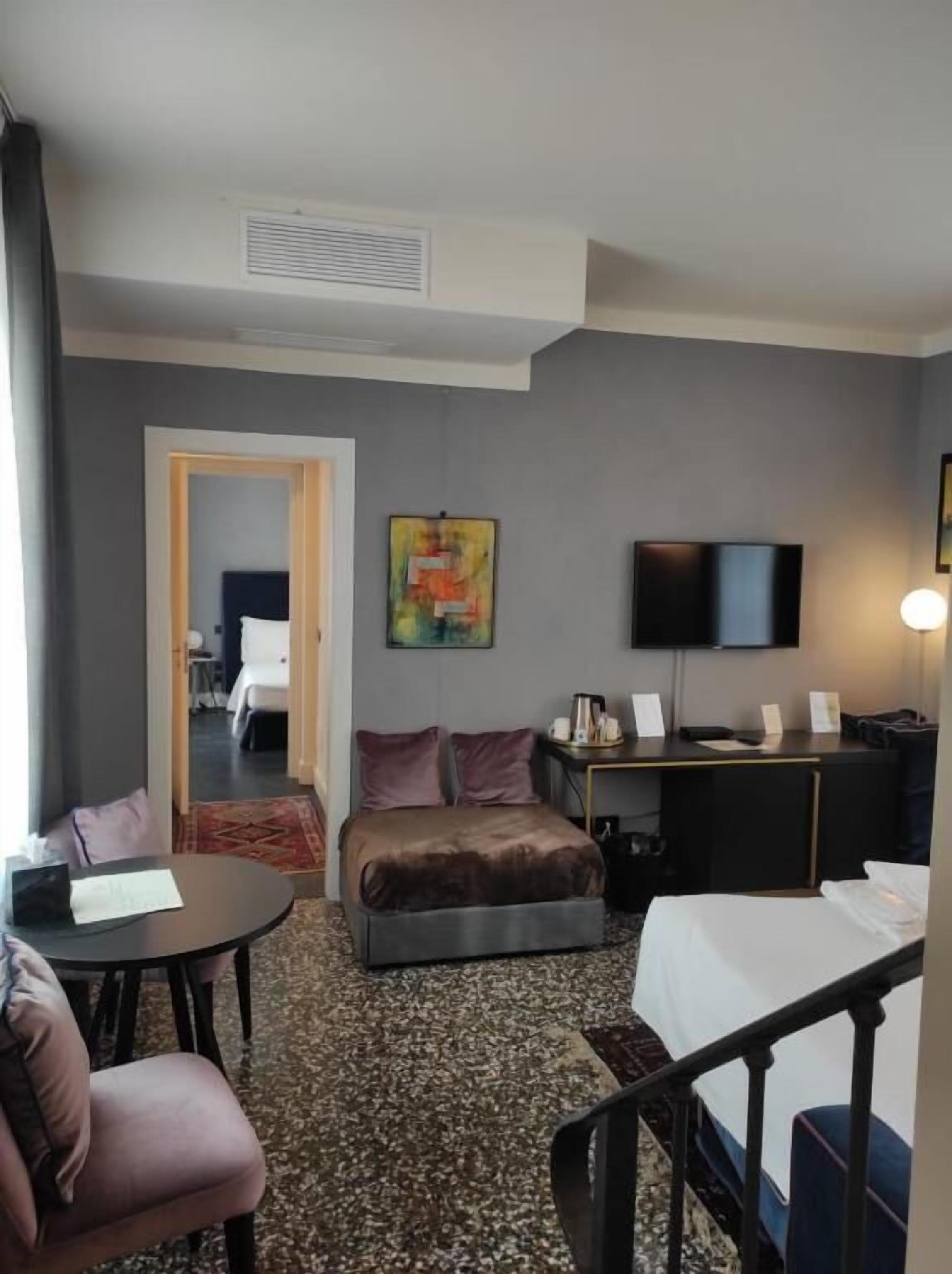 Una habitación de hotel con una cama, un escritorio con televisión de pantalla plana, una cafetera y un cuadro en la pared.