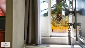 Entrada de una habitación de hotel con vista a un área de estar al aire libre, una puerta con llavero y una ventana con cortinas.